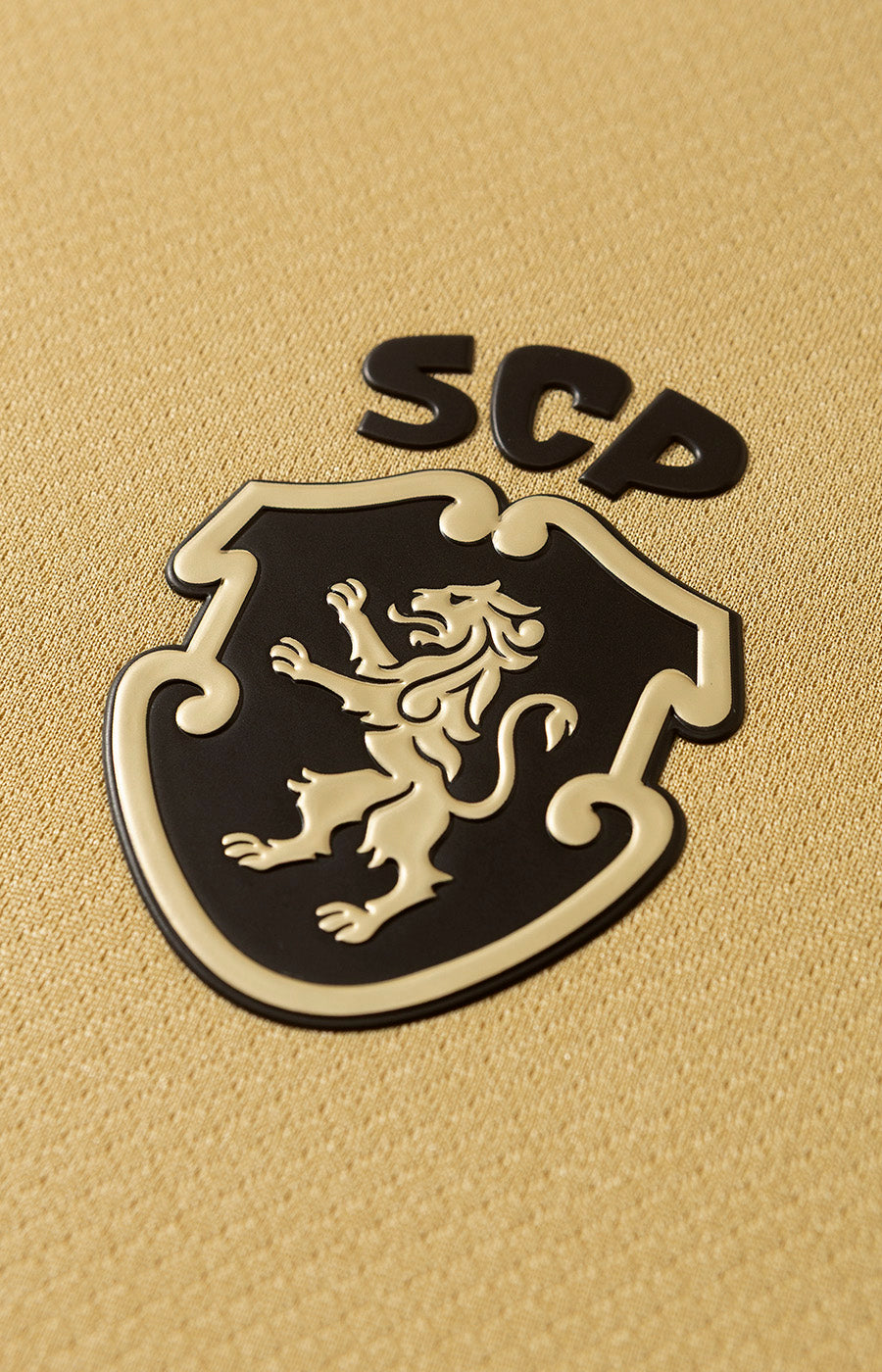Détail du nouvel écusson du Sporting Clube Portugal en relief noir et doré sur le maillot alternatif Total 90 du Sporting 26/27.
