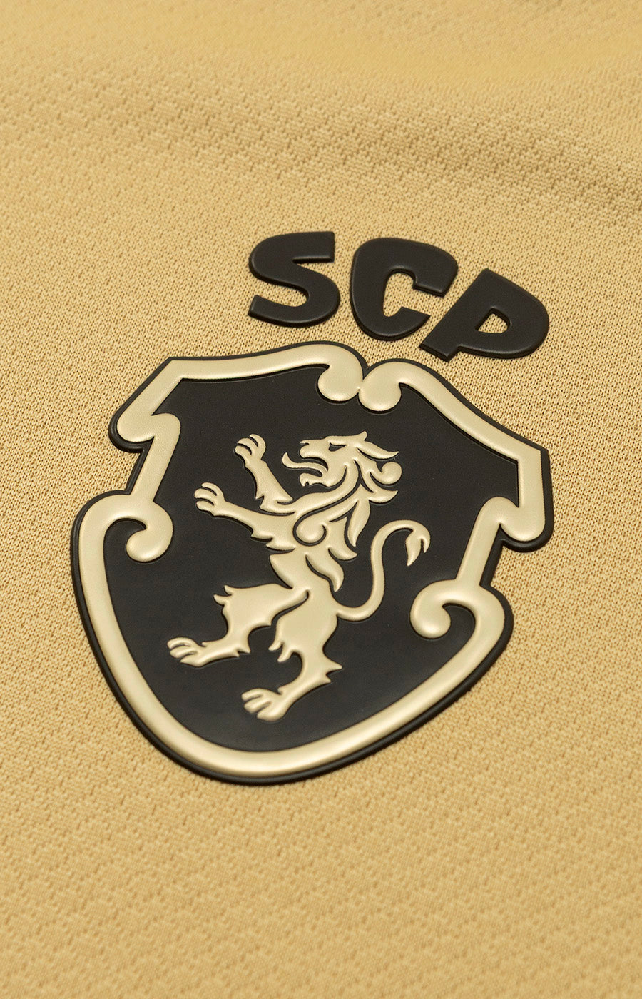 Pormenor do no emblema Sporting CP em relevo da Camisola Alternativa Dourada Total 90 26/27 de Mulher.
