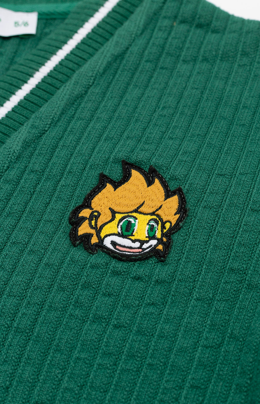 Detalhe da aplicação do Jubas no peito do cardigan verde do Sporting para criança.