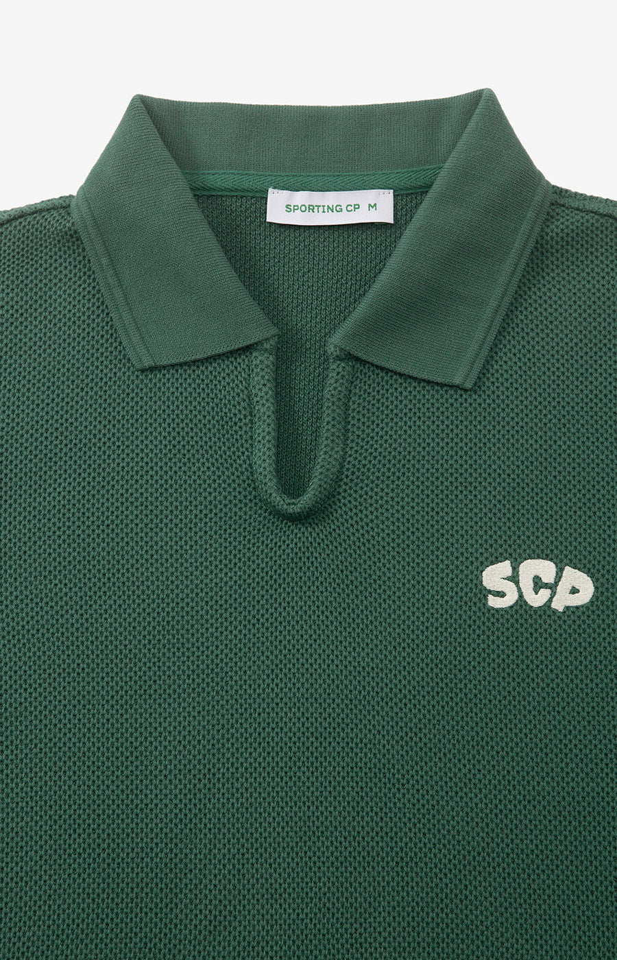 Pormenor da gola aberta e do decote em V do Polo Tricotado Verde do Sporting.