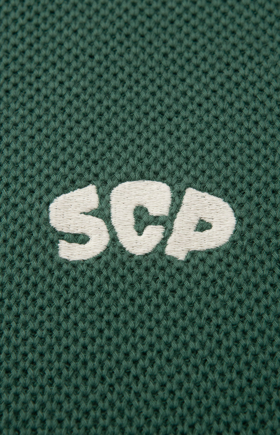 Pormenor das letras SCP aplicadas ao peito do Polo Tricotado Verde do Sporting.