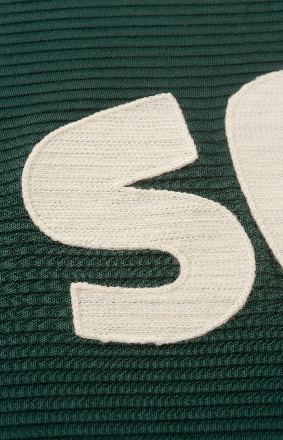 Pormenor das letras SCP aplicadas ao peito da Sweatshirt Verde do Sporting.