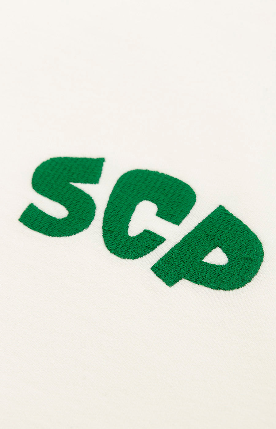 Détail des initiales « SCP » en vert sur la poitrine du sweat-shirt zippé blanc pour femme du Sporting.